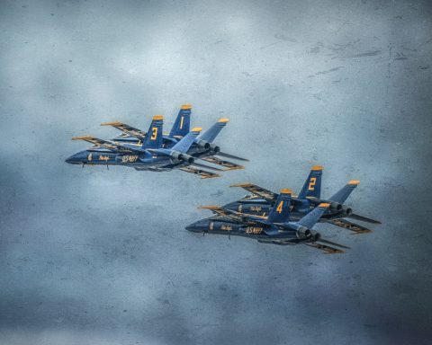 Four jet fighters in blue and yellow flying in formation against a cloudy sky.