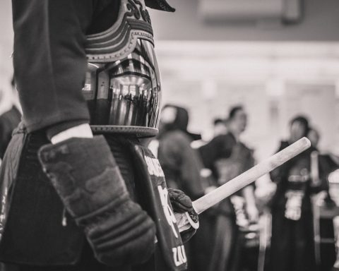 A kendo practitioner in armor holds a shinai, with others in the background.