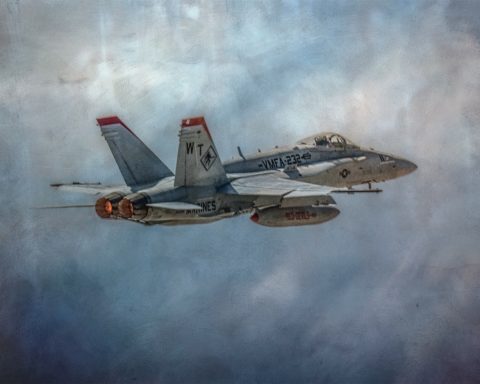 Fighter jet in flight with afterburners engaged against a cloudy sky.