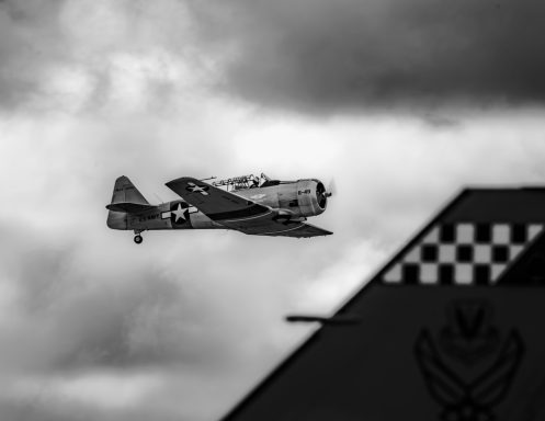 Vintage aircraft flying against a moody sky, with a checkered tail in the foreground.